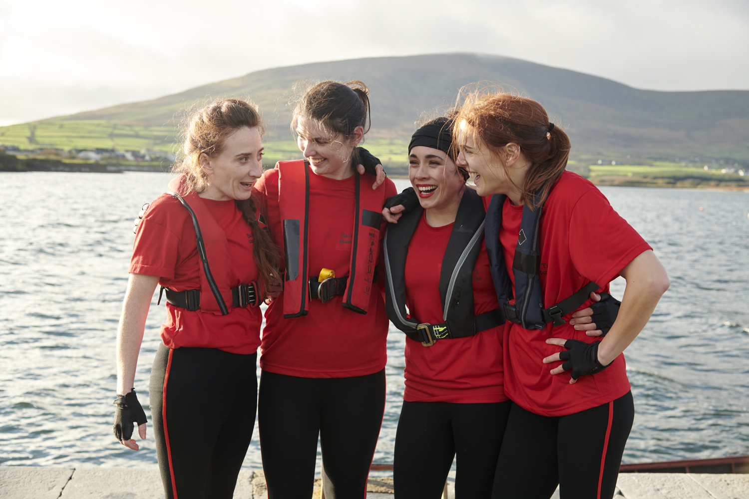 An image from the film Tarrac, showing five young women with red t-shirts and life jackets smiling as they stand by a lake